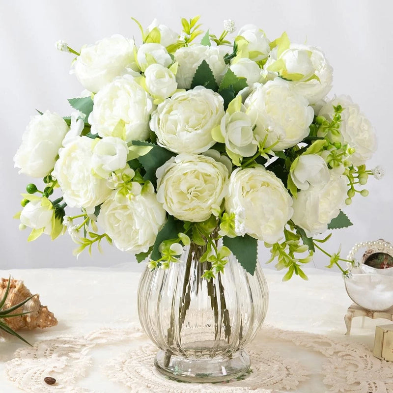 Artificial peony silk flower bouquet, white blooms and green leaves in clear glass vase