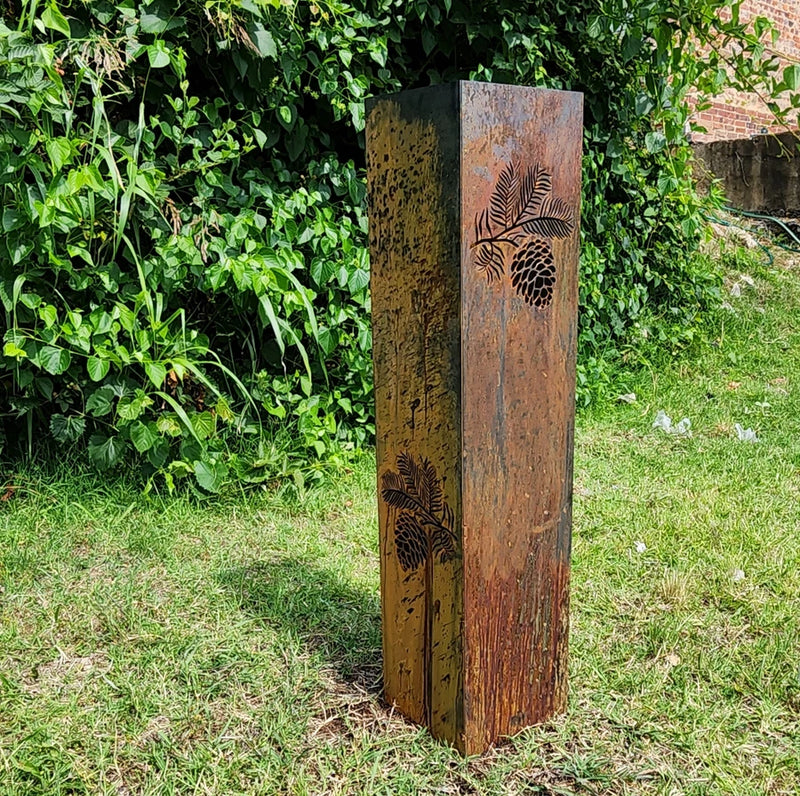 Rusty metal garden column statue with pinecone and leaf cutout design, textured finish