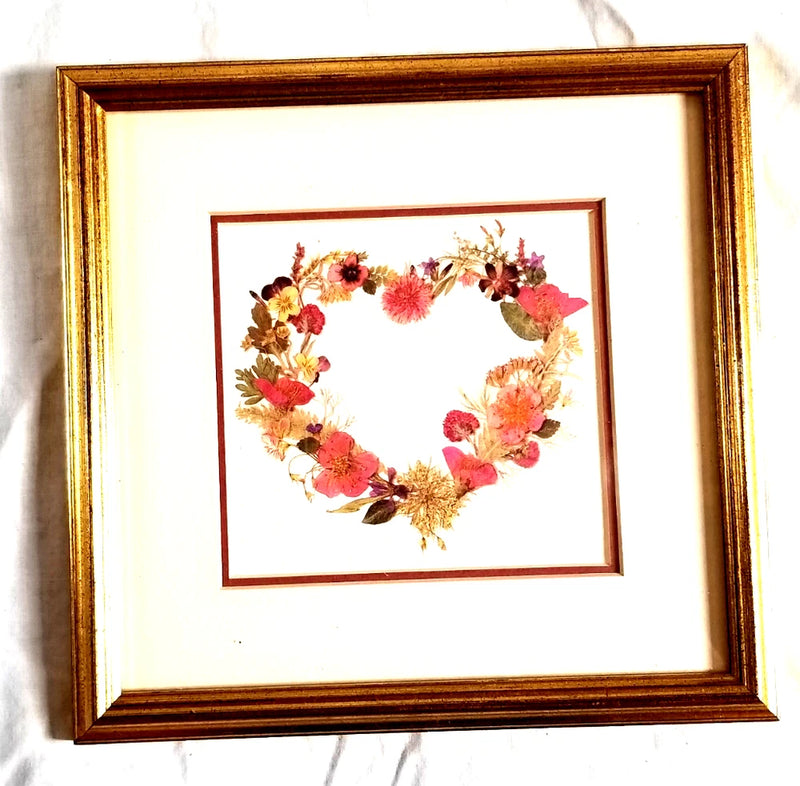 Framed pressed-flower heart wreath print with gold frame, floral wreath inside.