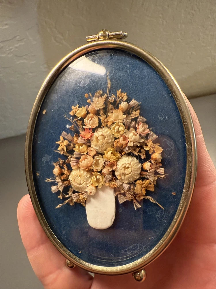 Curved oval frame with blue backing and dried flower bouquet under glass