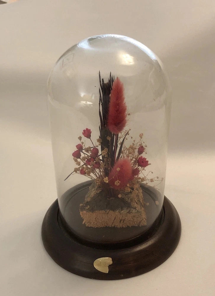 Dried flower cloche with clear glass dome and dark wooden base, red and pink blooms inside