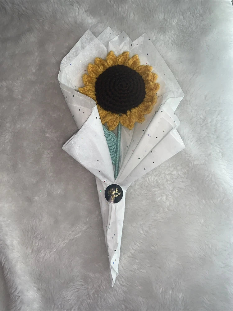 Crocheted sunflower artificial flower bouquet with green stem, wrapped in white paper.