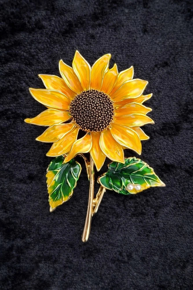 Sunflower brooch with yellow petals, dark center, green leaves and gold-tone pin