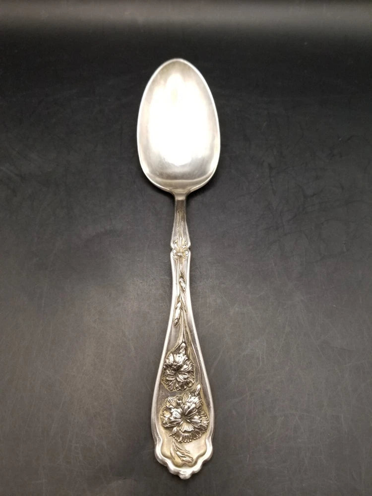 Antique silver serving spoon with ornate floral engraving on handle