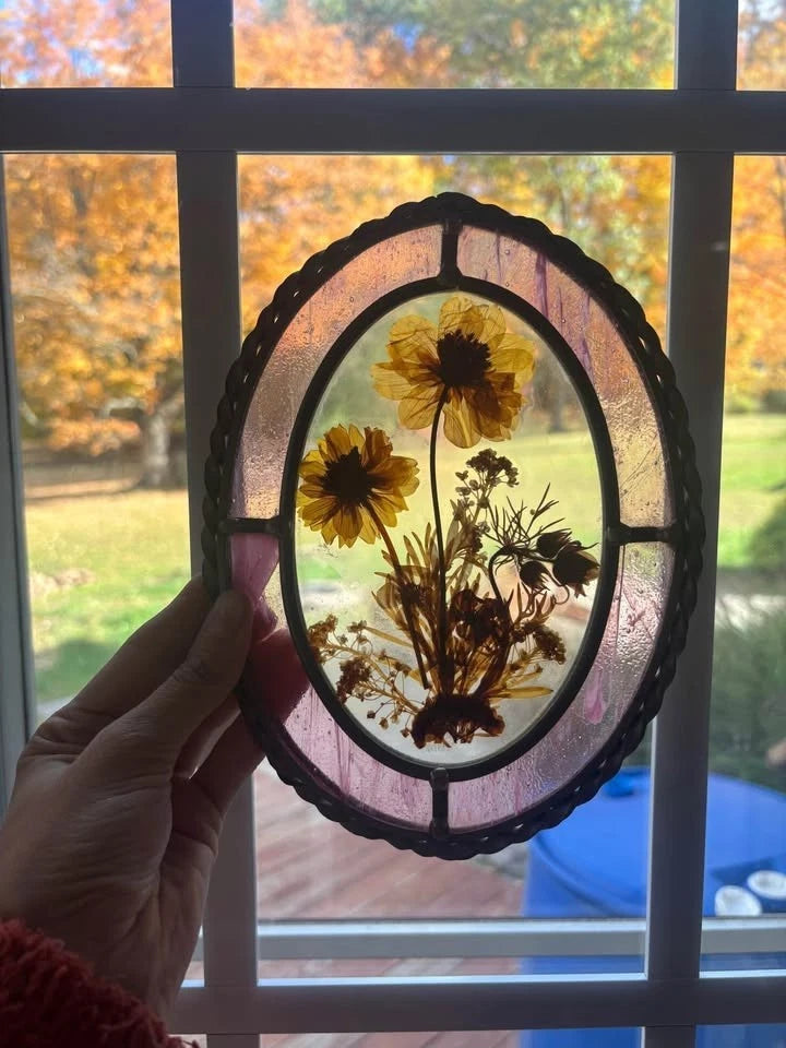 Oval framed glass suncatcher with pressed yellow dried flowers inside black border