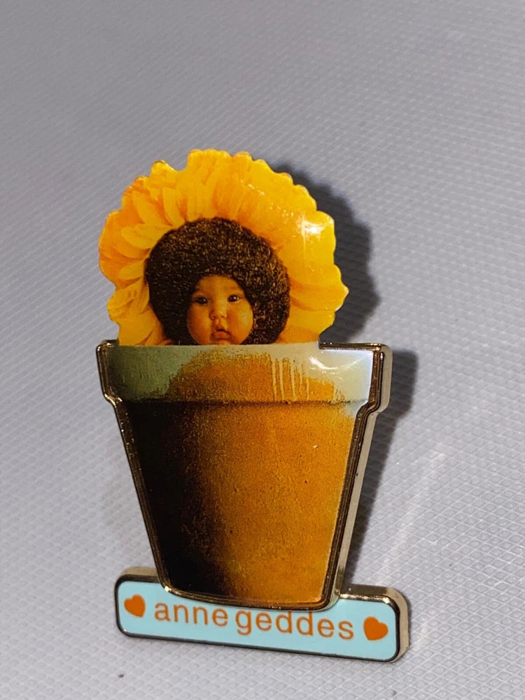 Sunflower lapel pin with baby in brown flower pot and anne geddes logo