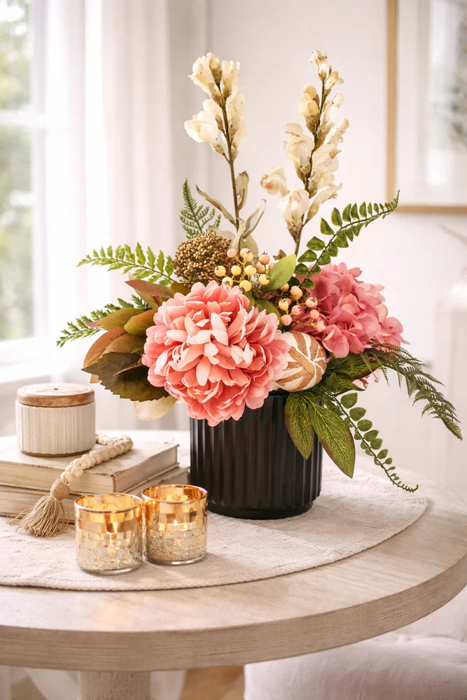 Small floral peony arrangement in dark ceramic vase with peach and pink blooms and greenery