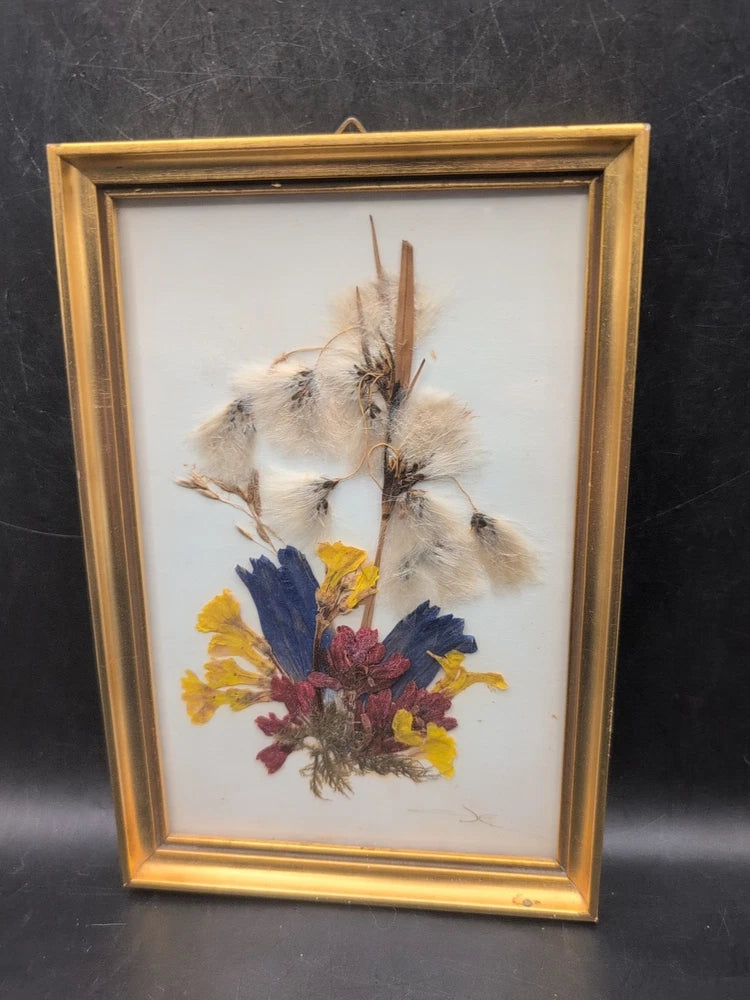 Gold-framed dried flower art with white feathers and yellow, blue, and red blooms