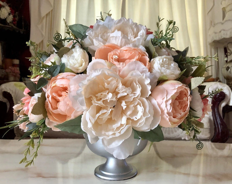 Peony floral centerpiece with blush peach and white blooms and green foliage on pedestal