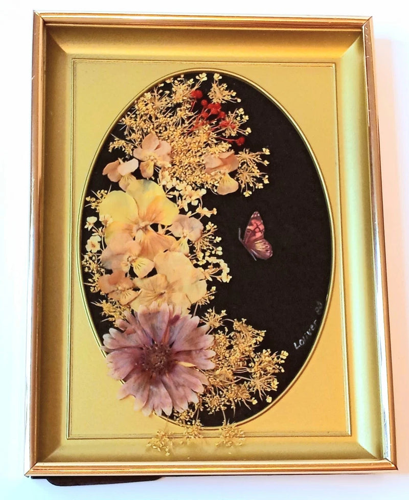 Oval glass-framed pressed dried flowers with butterfly motif, dark background