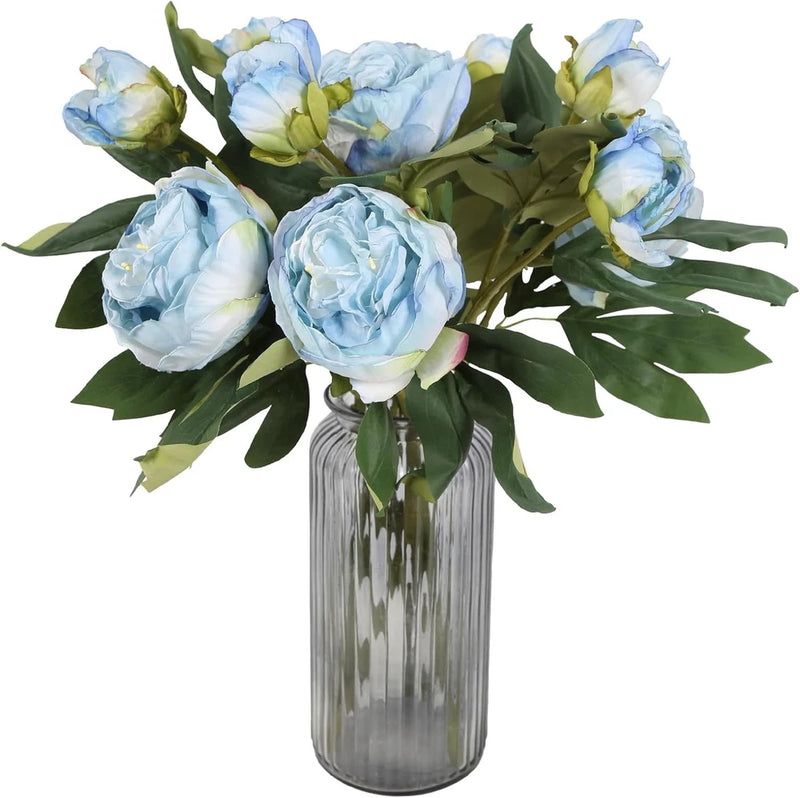 Artificial blue peony flower bouquet in clear ribbed glass vase with green leaves