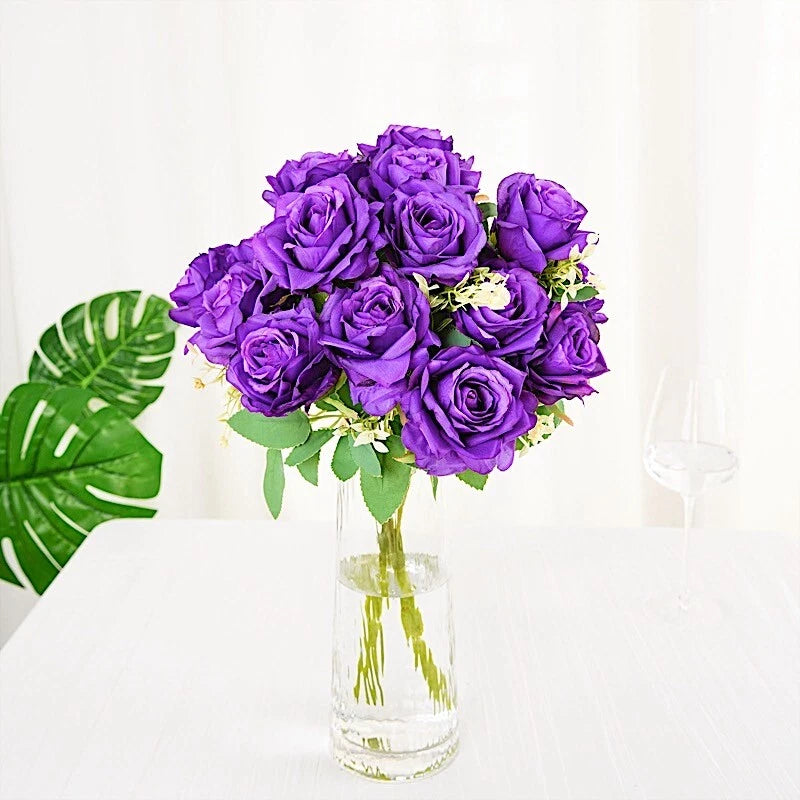 Purple artificial silk rose bouquet with green leaves in a clear glass vase