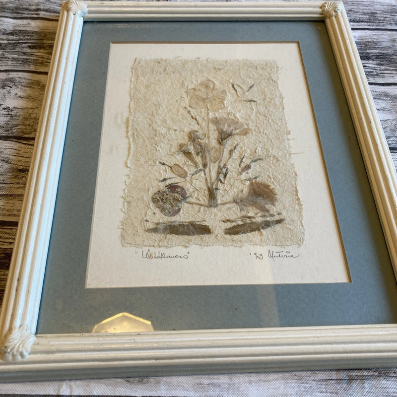 Framed pressed dried wildflowers under glass, beige tones, artist signature at bottom