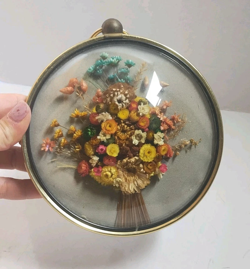 Round dried flower wall art with gold frame and glass dome, mixed bouquet inside.