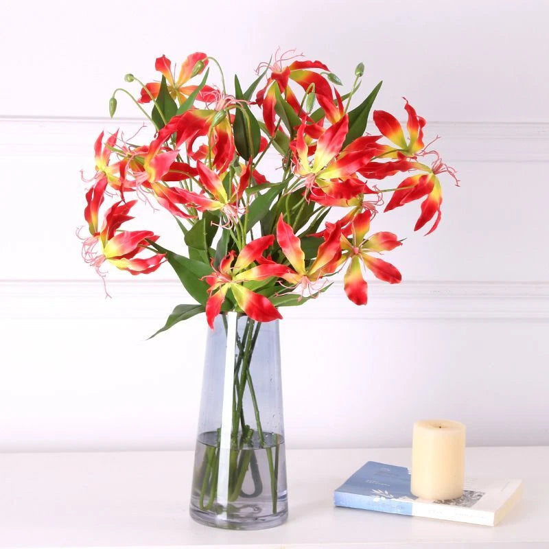 Artificial lily flower arrangement in clear glass vase with red and yellow blooms