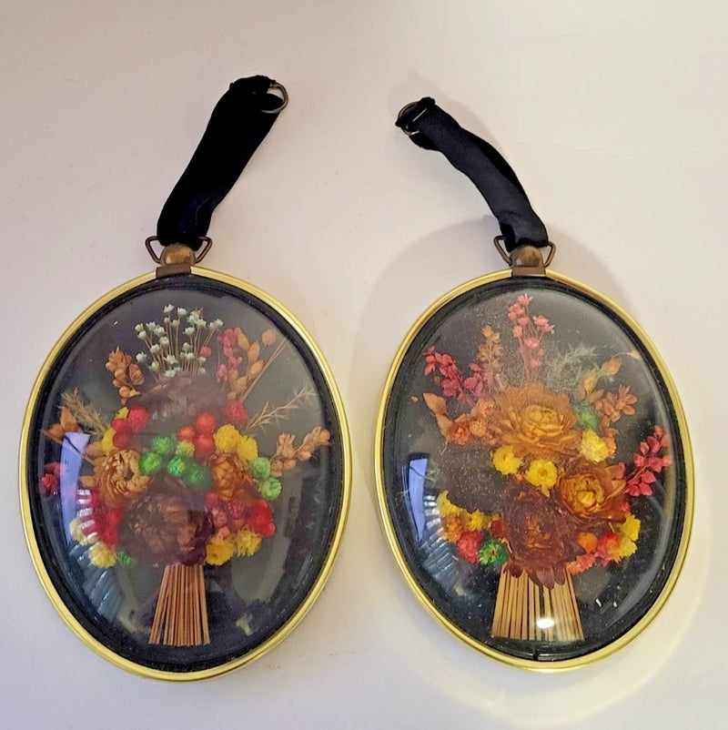 Pair of oval domed glass hanging frames with dried flower bouquets and black straps