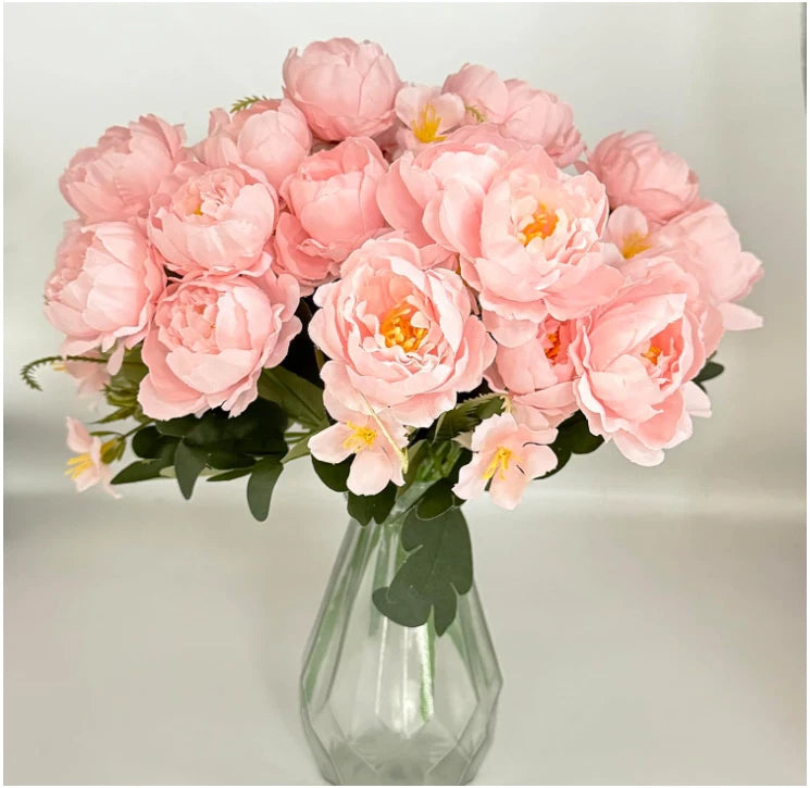 Pink faux peony bouquet with green leaves in clear glass vase