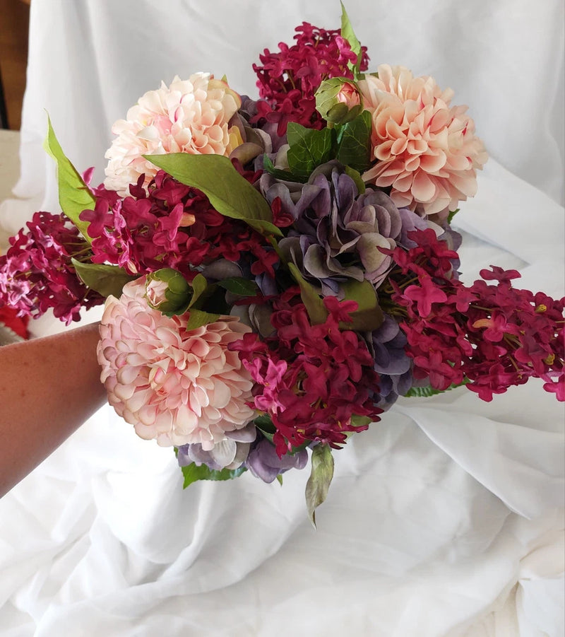 Handmade bridal bouquet with purple, burgundy, and blush pink flowers and green leaves
