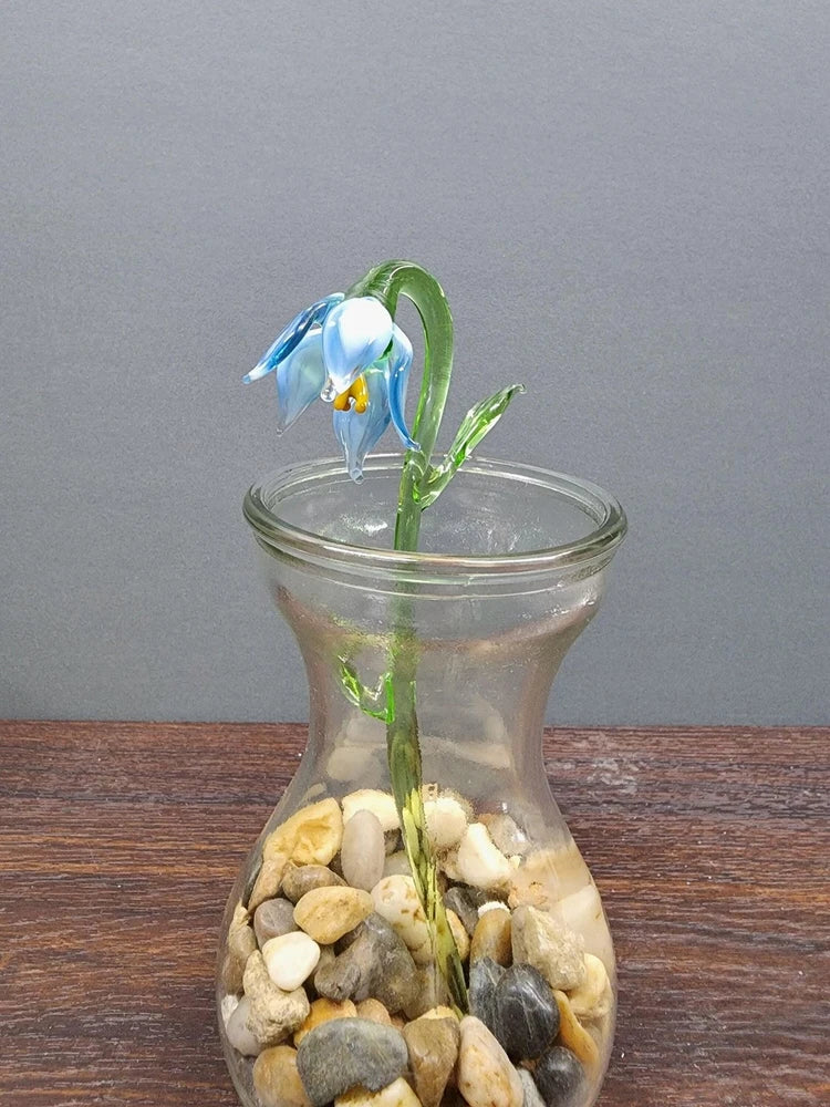 Handcrafted glass lily flower in clear vase with mixed stones and petals, blue and green