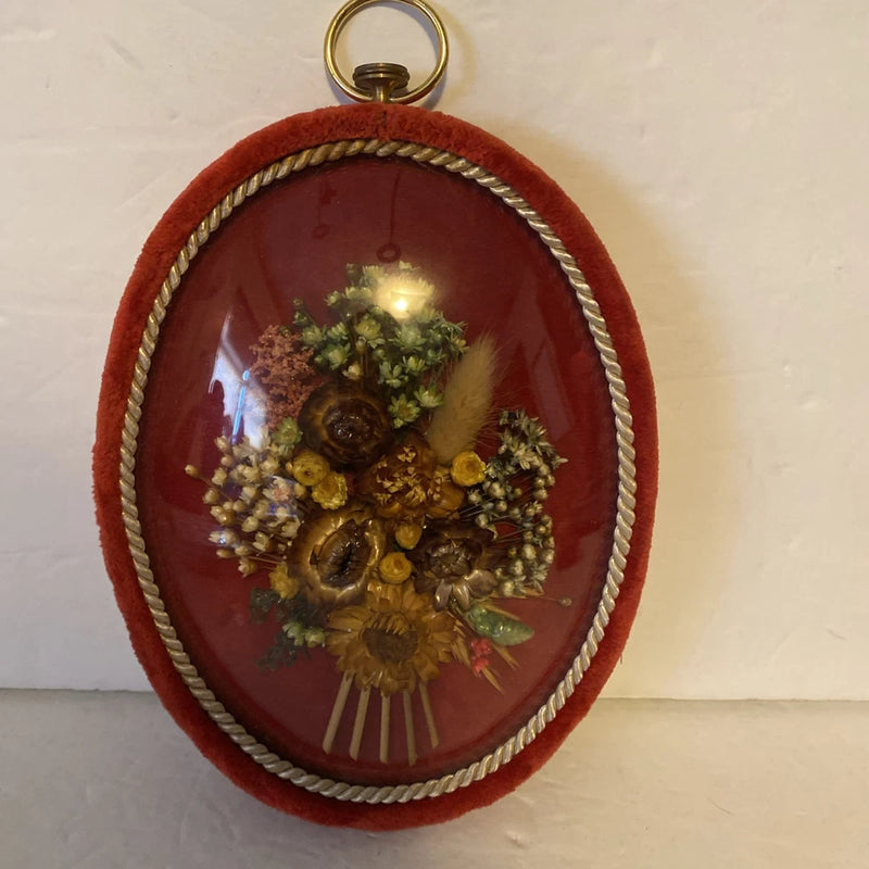 Oval dried flower wall art with convex glass dome, red fabric frame, gold braided edge
