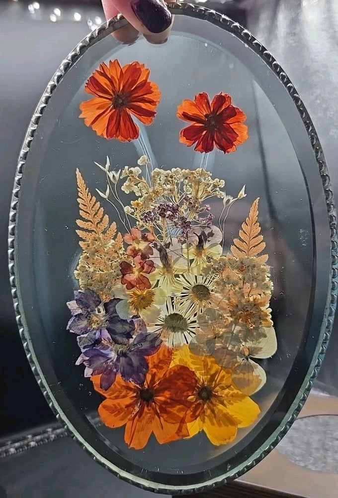 Oval glass suncatcher with soldered metal rim, pressed orange, purple, and yellow flowers.