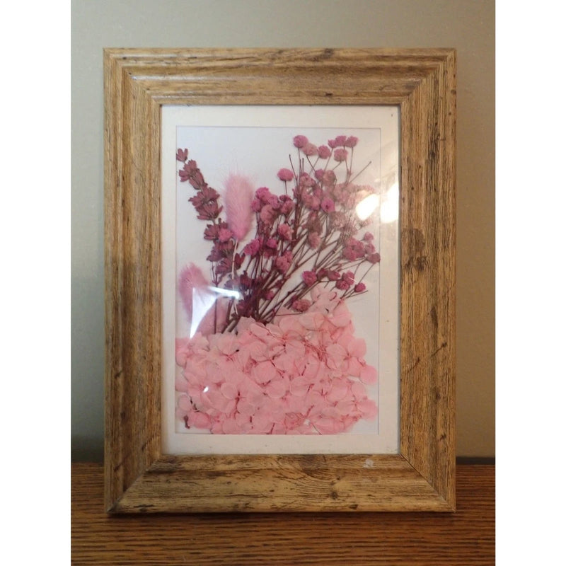 Framed dried flower wall art with pink pressed blossoms in a rustic wooden frame