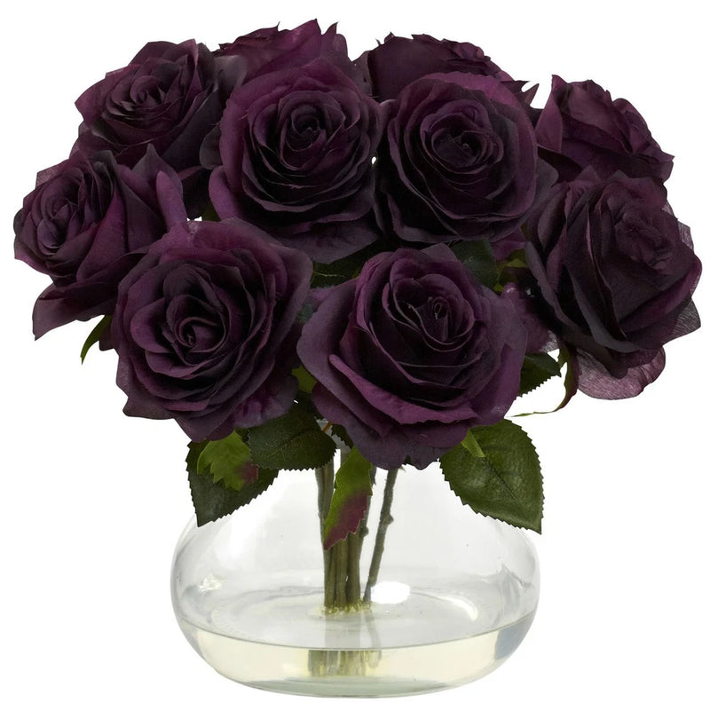 Purple artificial rose bouquet in clear glass vase with green leaves