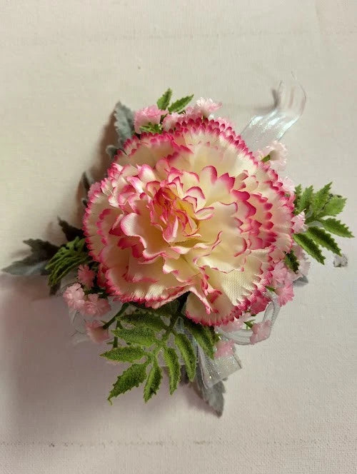 Pink carnation wrist corsage with ruffled petals, green leaves, and sheer tulle band
