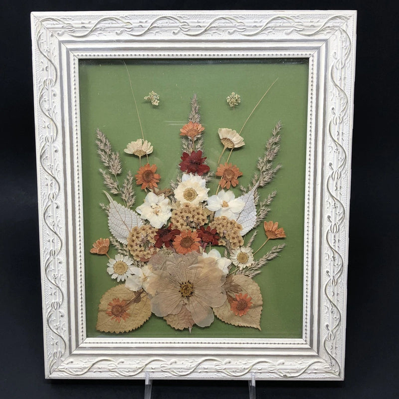 Distressed white framed pressed flower wall art with dried florals on green backdrop
