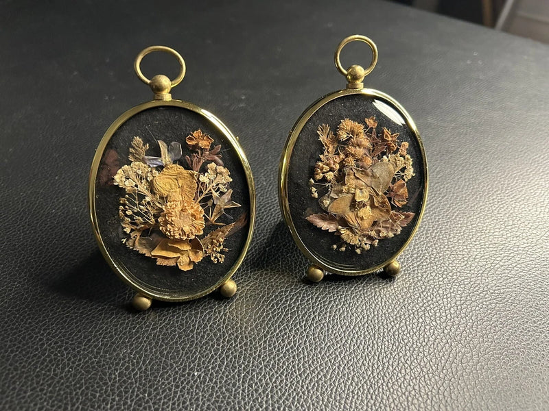 Pair of oval bubble glass dried flower pendants in brass-tone frames with loop tops