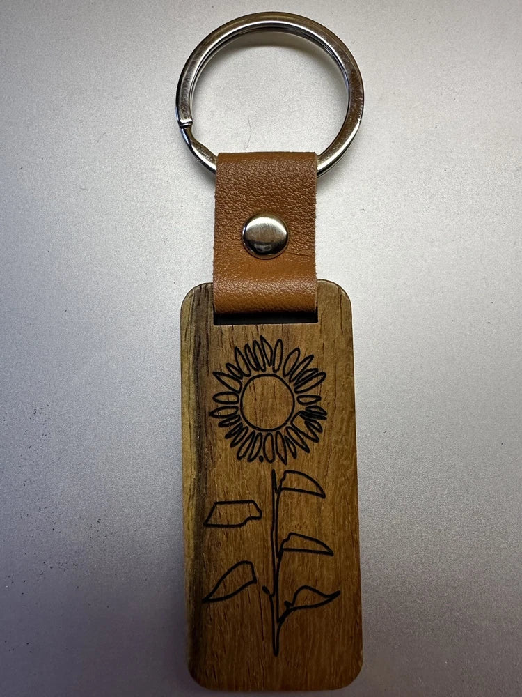 Sunflower keychain with wooden charm, brown leather strap, and metal key ring.