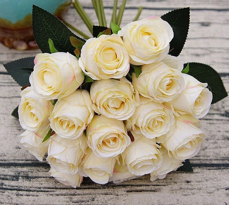 Artificial rose bouquet with pale cream blooms and dark green leaves, wedding decor style