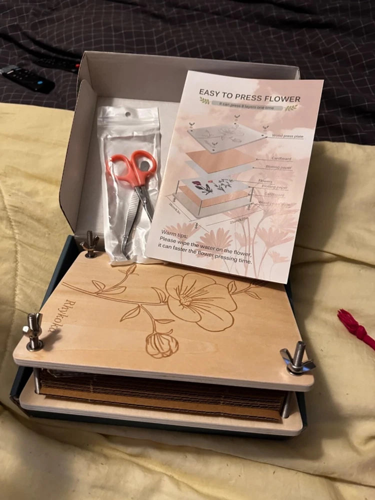 Wooden flower press with metal clamps and stacked boards, open with tools and instructions