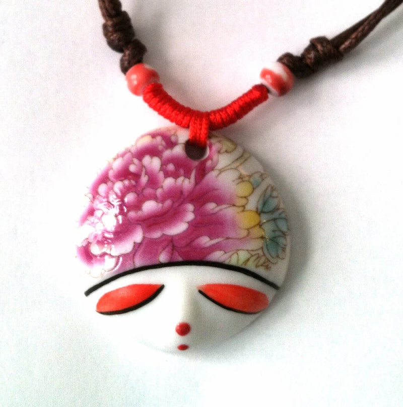 Ceramic face pendant choker necklace with red cord and pink peony-style floral design