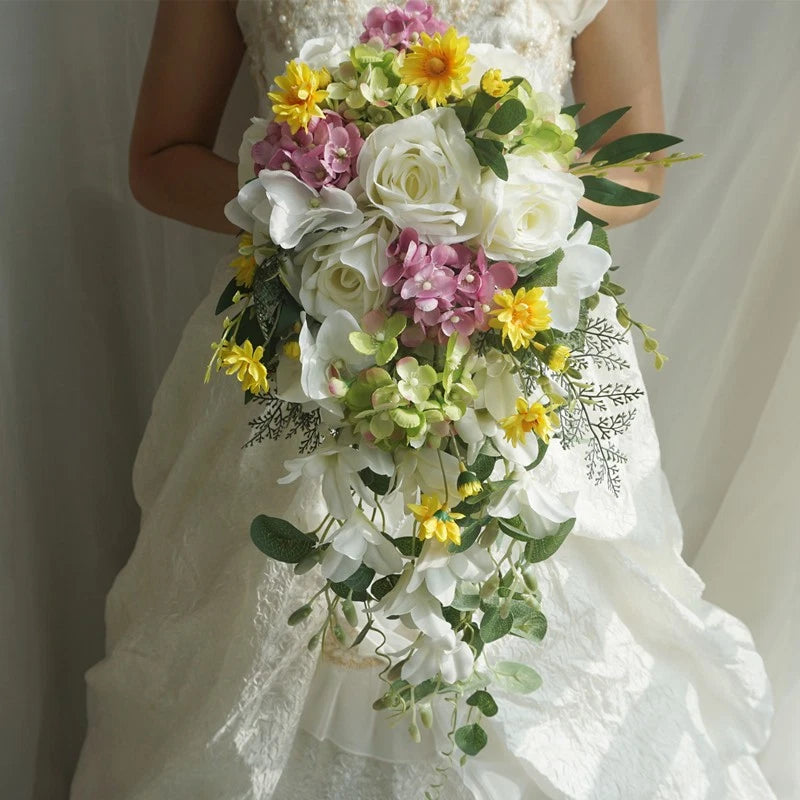 Cascade-style wedding bouquet with white roses, pink and yellow blooms, and green greenery