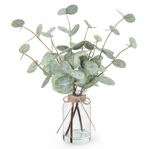 Artificial eucalyptus stems in clear glass vase with green lifelike leaves