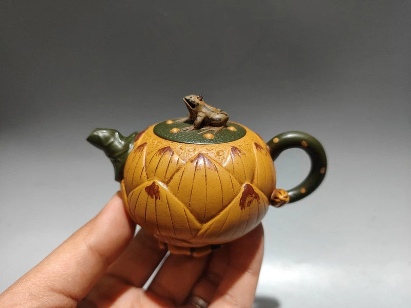 Handheld ceramic teapot with frog lid, rounded body, green handle and spout