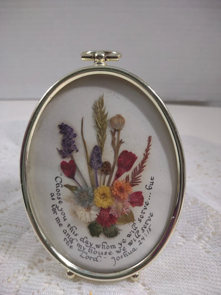 Oval metal frame with pressed dried flowers and handwritten scripture text around the border