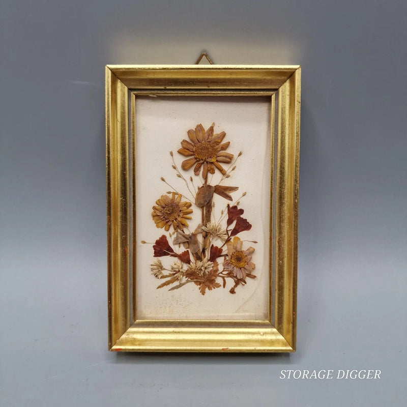 Gold-tone framed pressed dried flower artwork with small brown and burgundy blooms