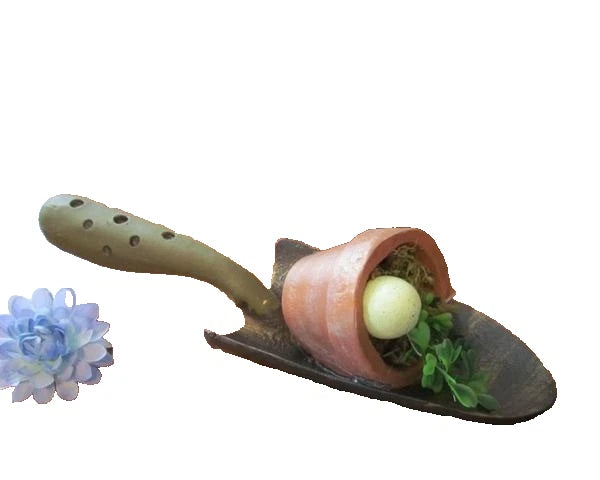 Garden trowel figurine holding a bird nest with green plants and an egg