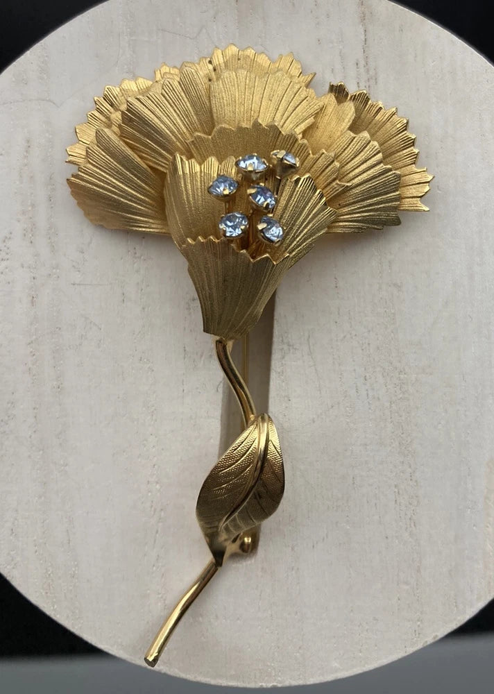 Gold-tone floral brooch with blue rhinestone cluster and leaf pin stem