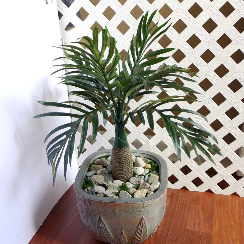 Artificial potted small tree plant with long green leaves, gray textured pot and rocks