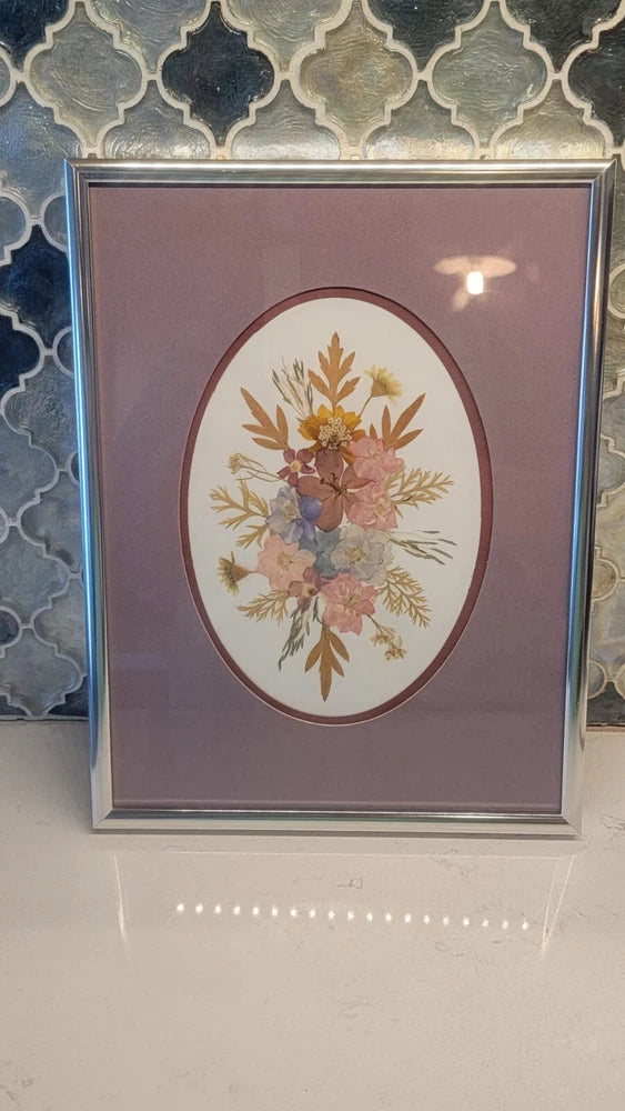 Vintage framed pressed flower art with oval floral arrangement, purple background