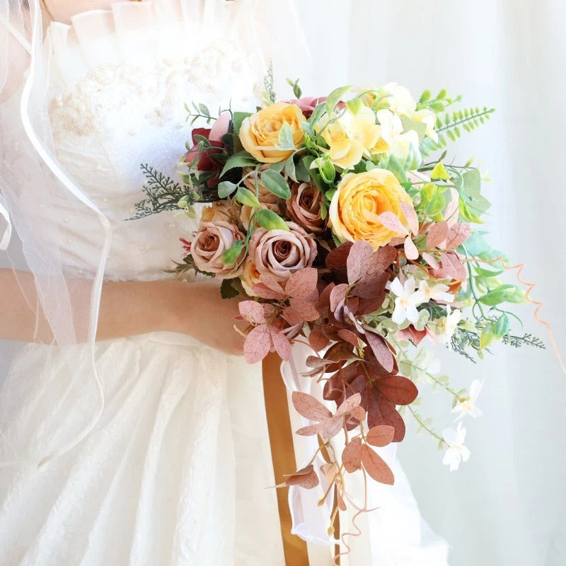 Pastel rose bridal bouquet with orange and pink blooms, green leaves, and trailing greenery
