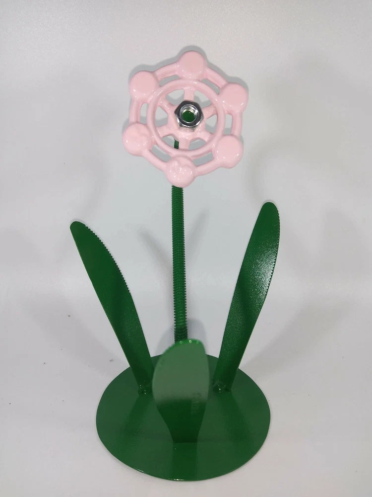 Pink metal flower with green stems and leaves on round display base