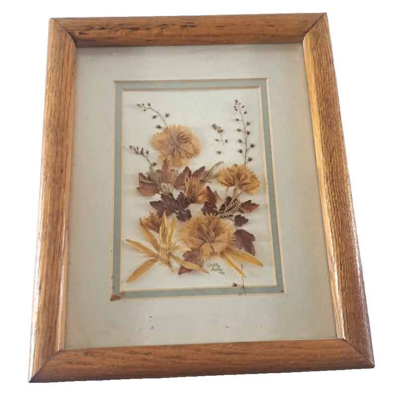 Framed pressed dried flower artwork with tan blossoms and leaves in wooden frame