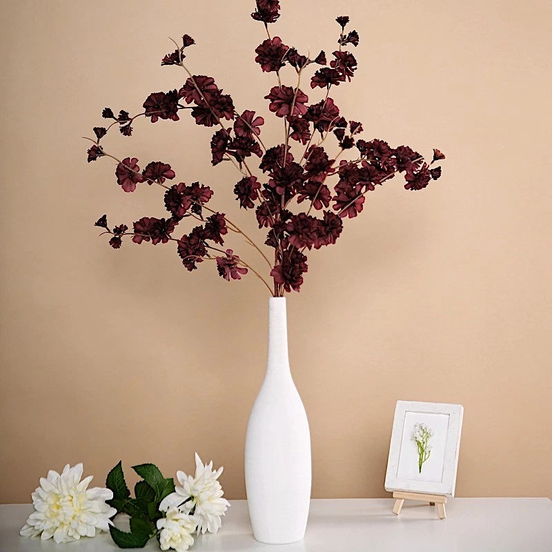 Artificial silk carnation flower sprays with burgundy stems, shown in a white vase
