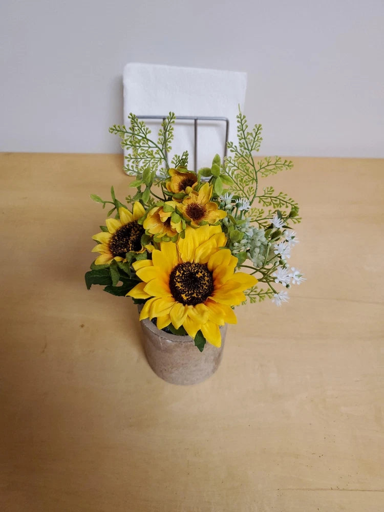 Artificial sunflower flower arrangement in gray pot with yellow blooms and green foliage