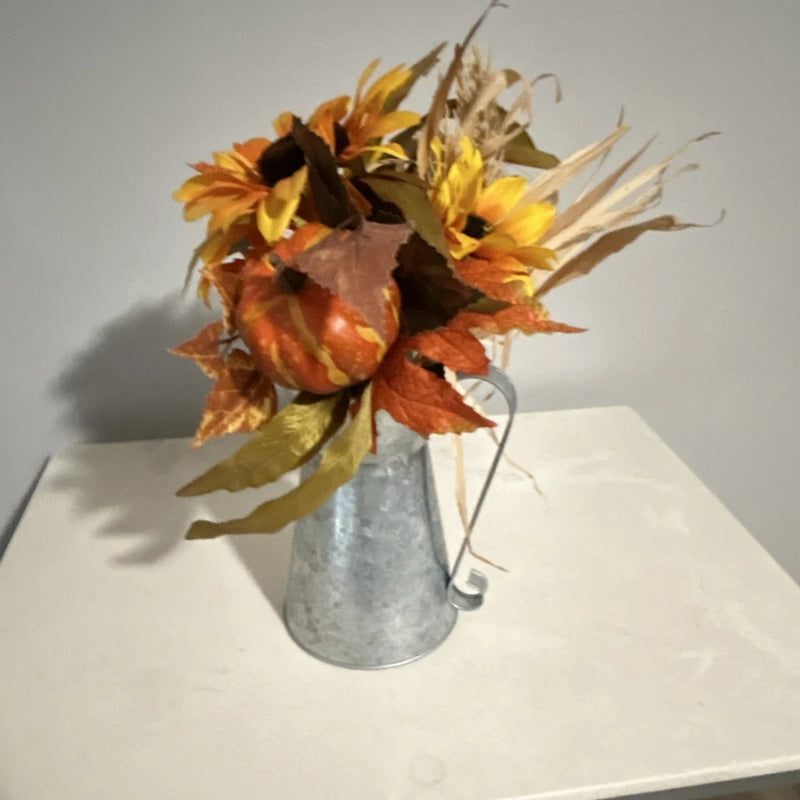 Artificial sunflower arrangement in metal vase with yellow-orange blooms and autumn leaves