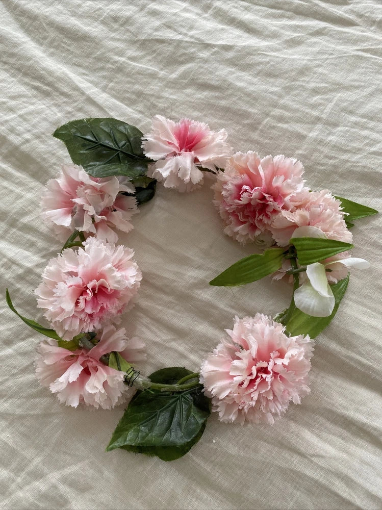 Pink carnation flower headband with five blooms and green leaves on a white ribbon